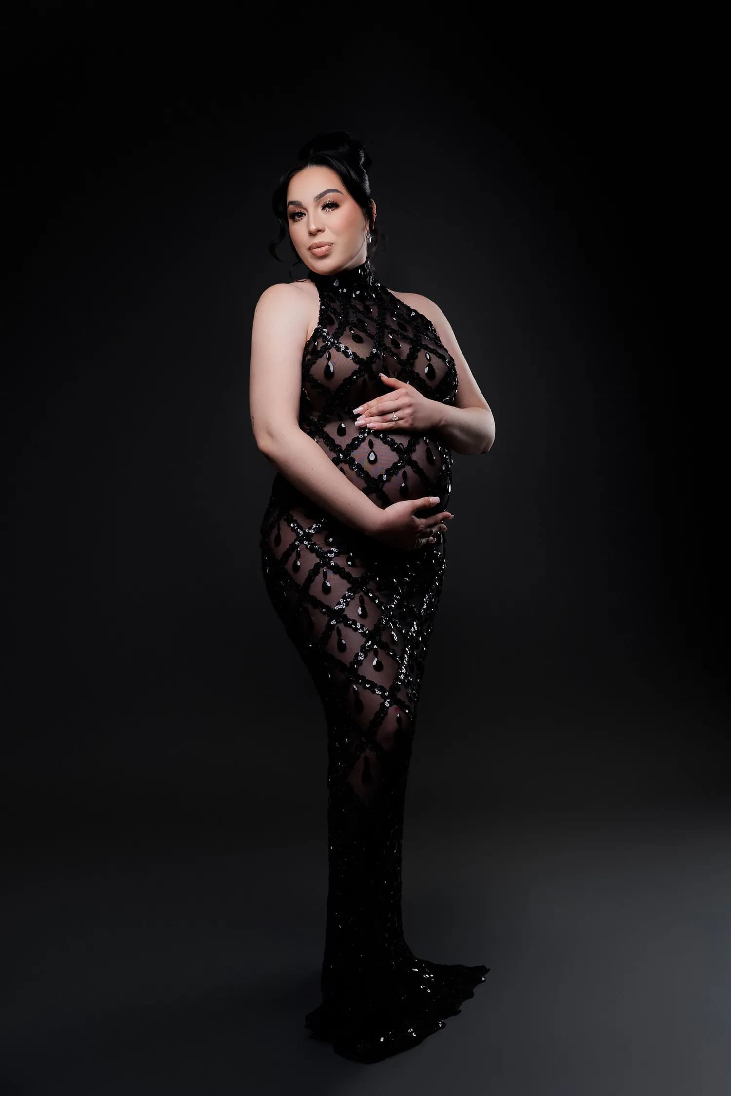 Pregnant woman in a black beaded lace gown against a dark studio backdrop