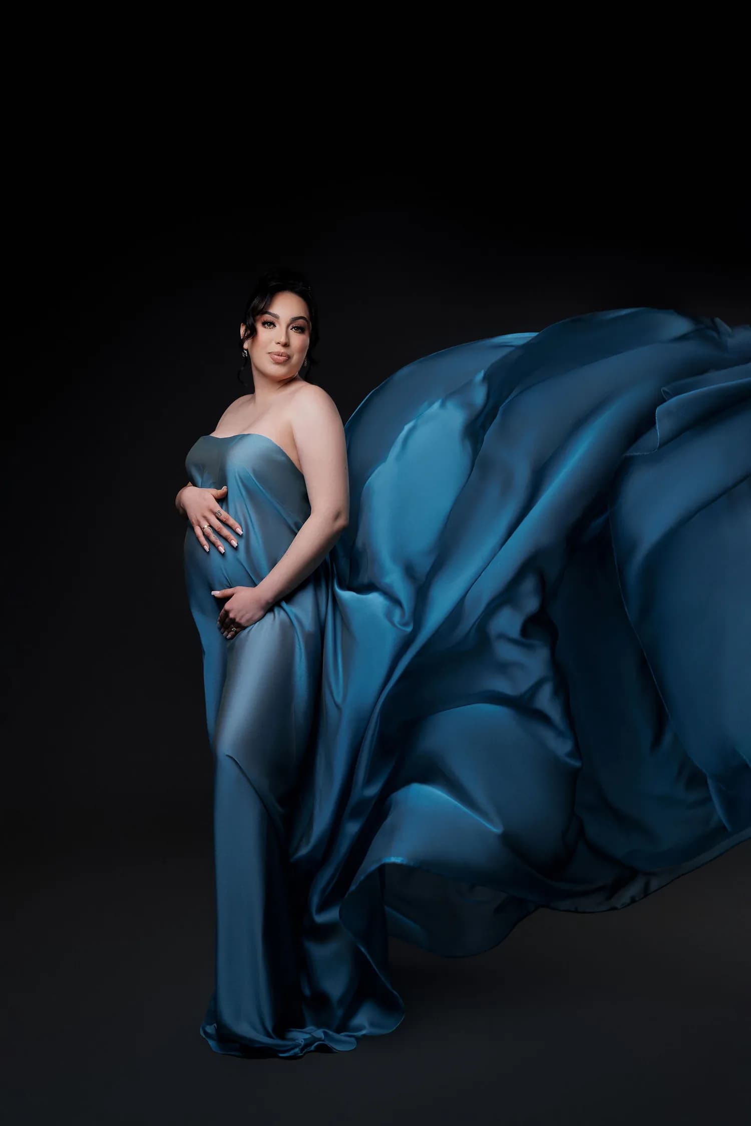 Pregnant woman in blue satin with the fabric flowing out behind her