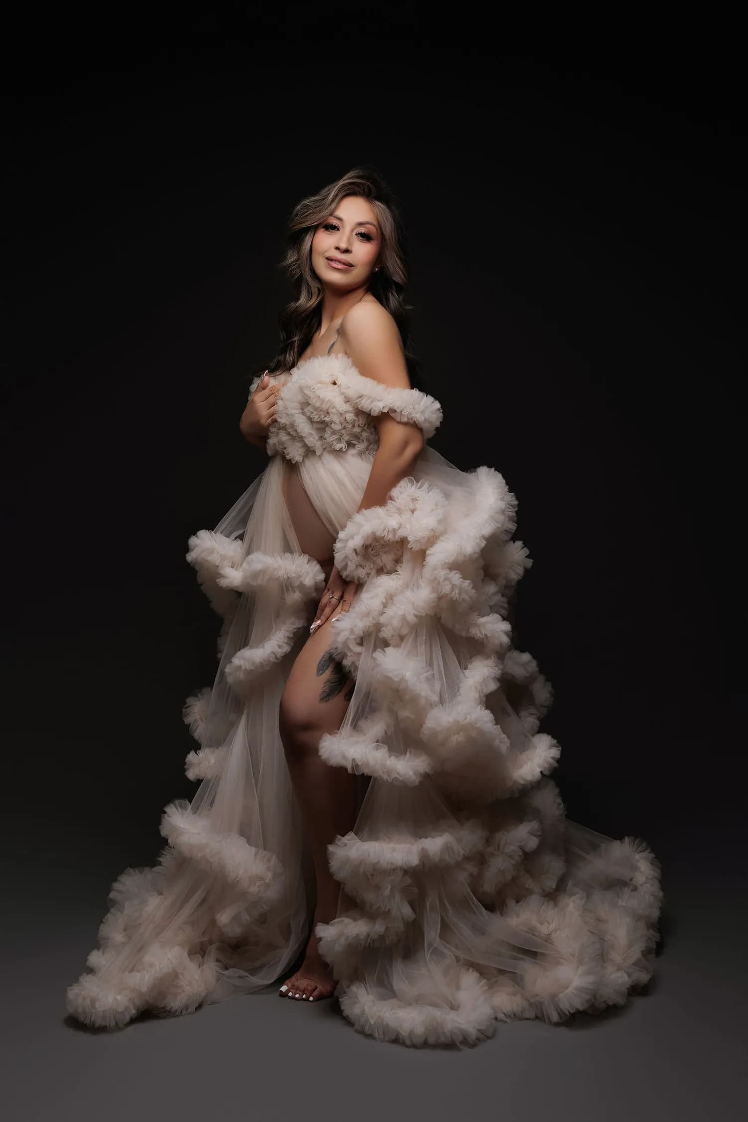 Pregnant woman in a blush ruffled tulle gown, turned to one side