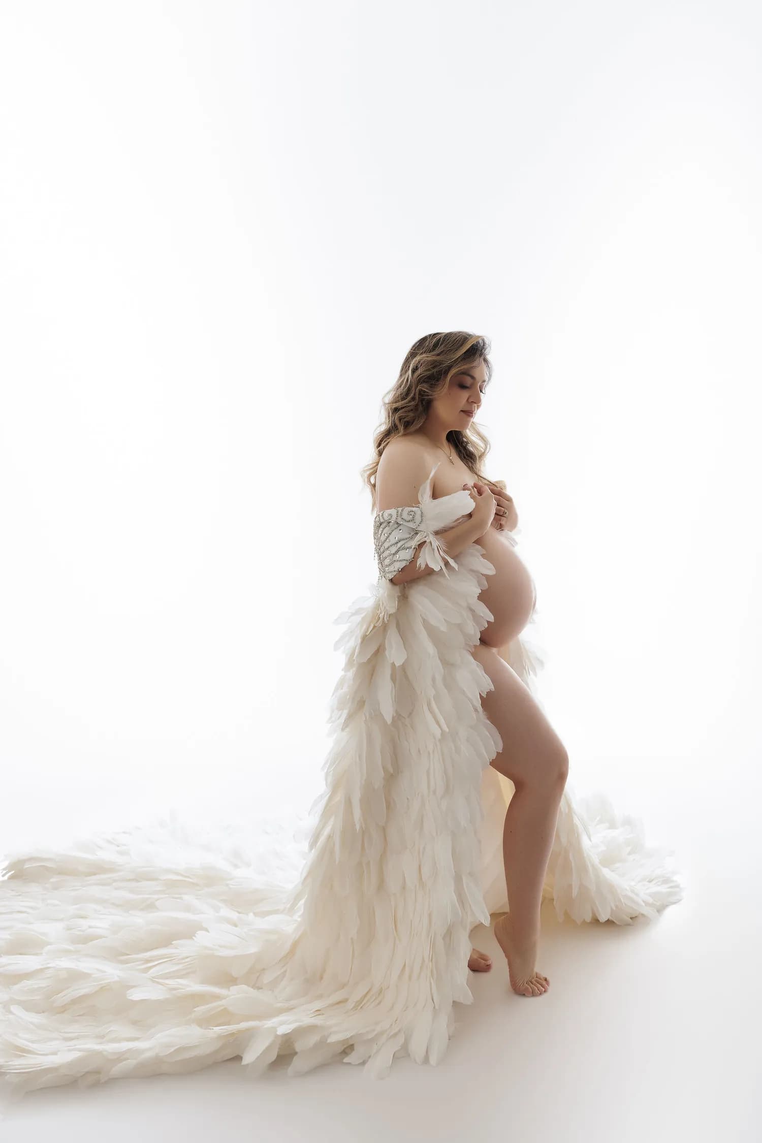 Pregnant woman in an ivory feather gown with a long train on a white background