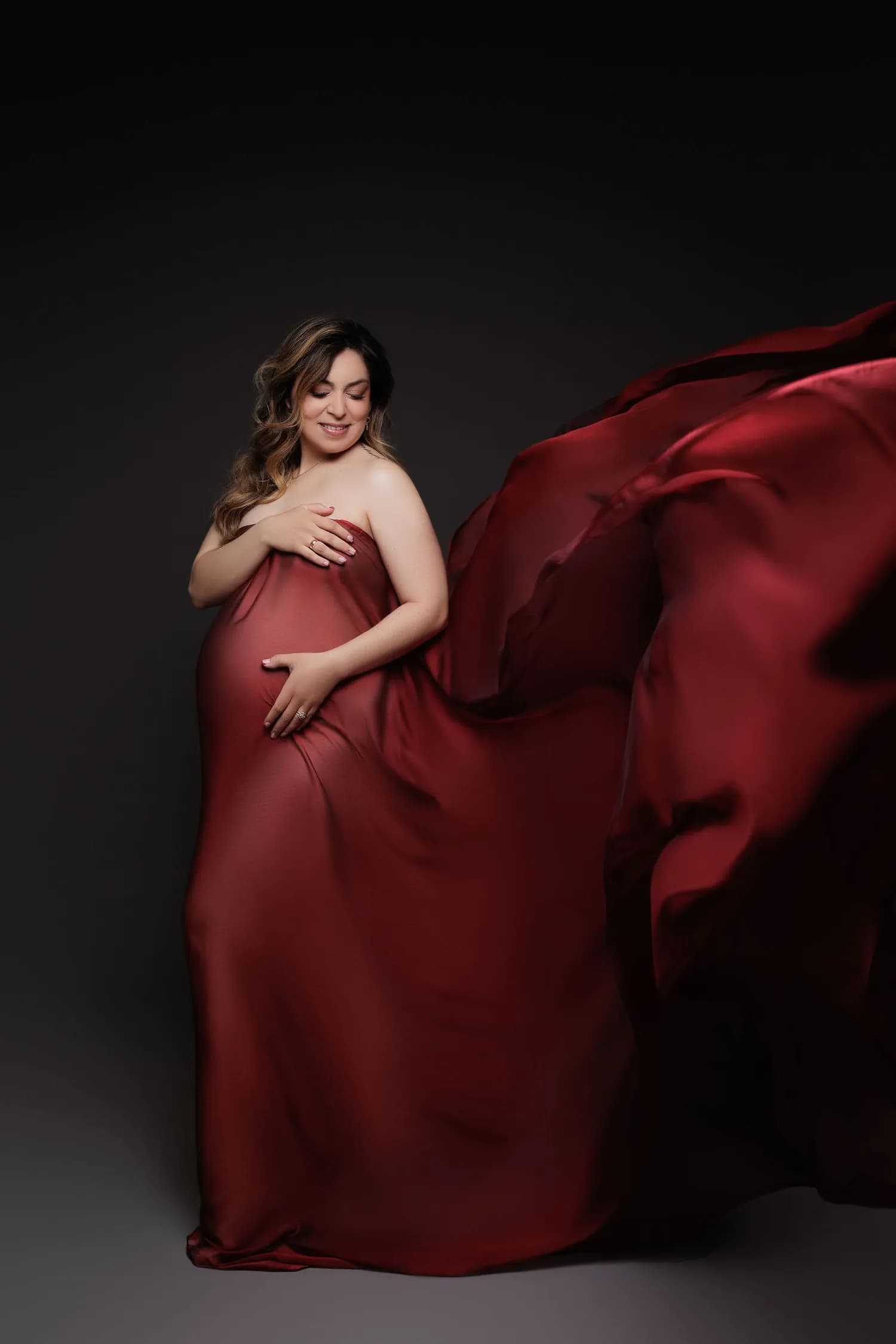 Pregnant woman wrapped in red satin that sweeps out behind her