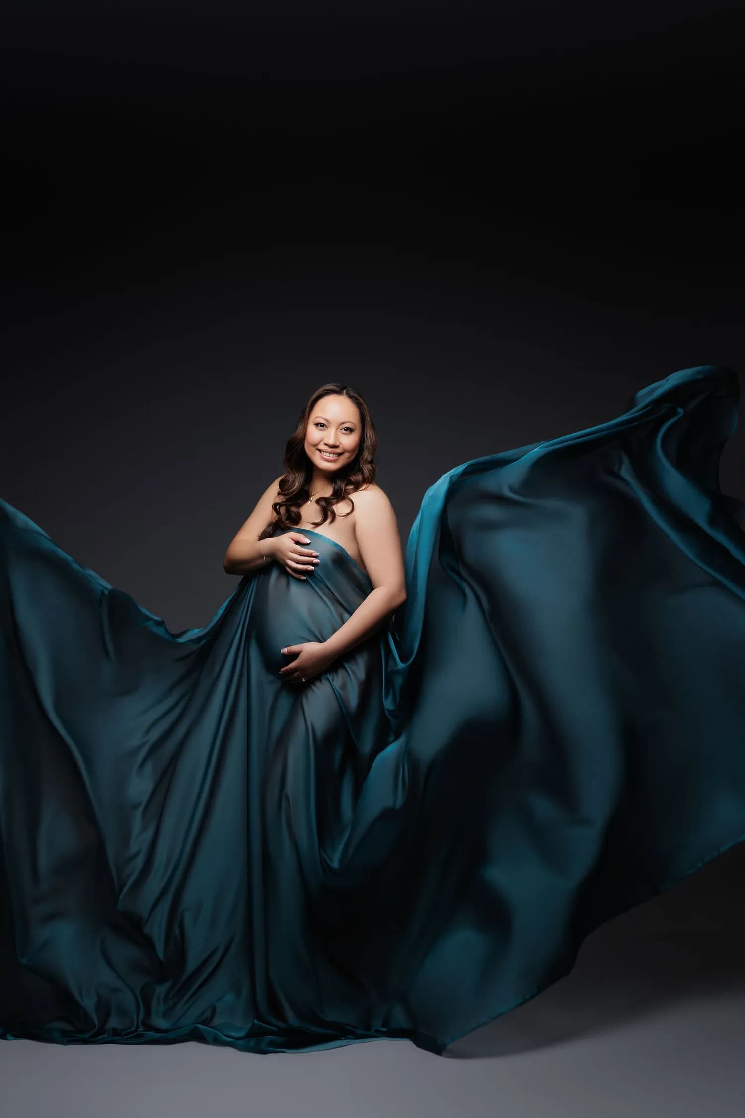 Pregnant woman in teal satin with the fabric spread wide like wings