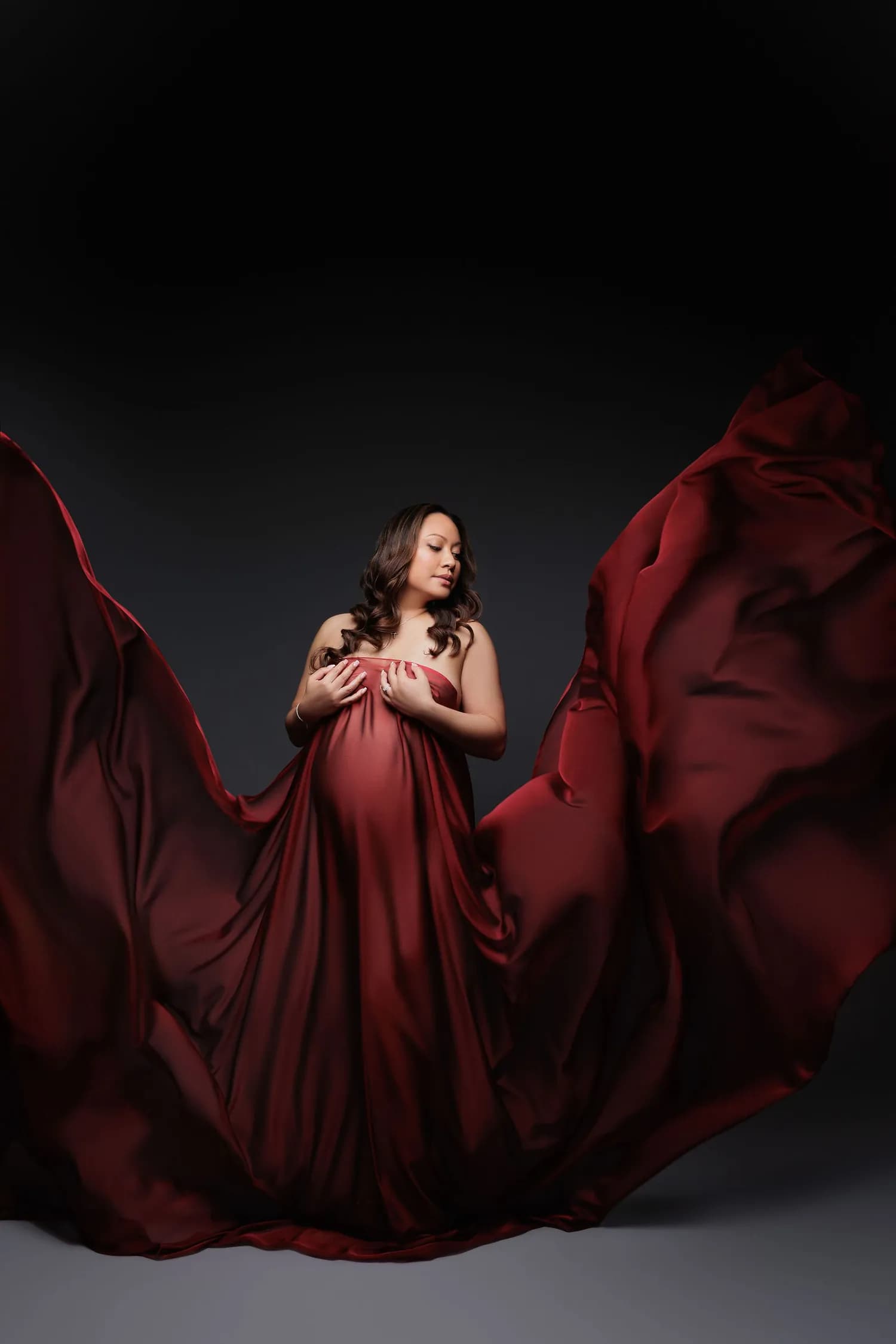 Pregnant woman in deep red satin with the fabric spread wide like wings