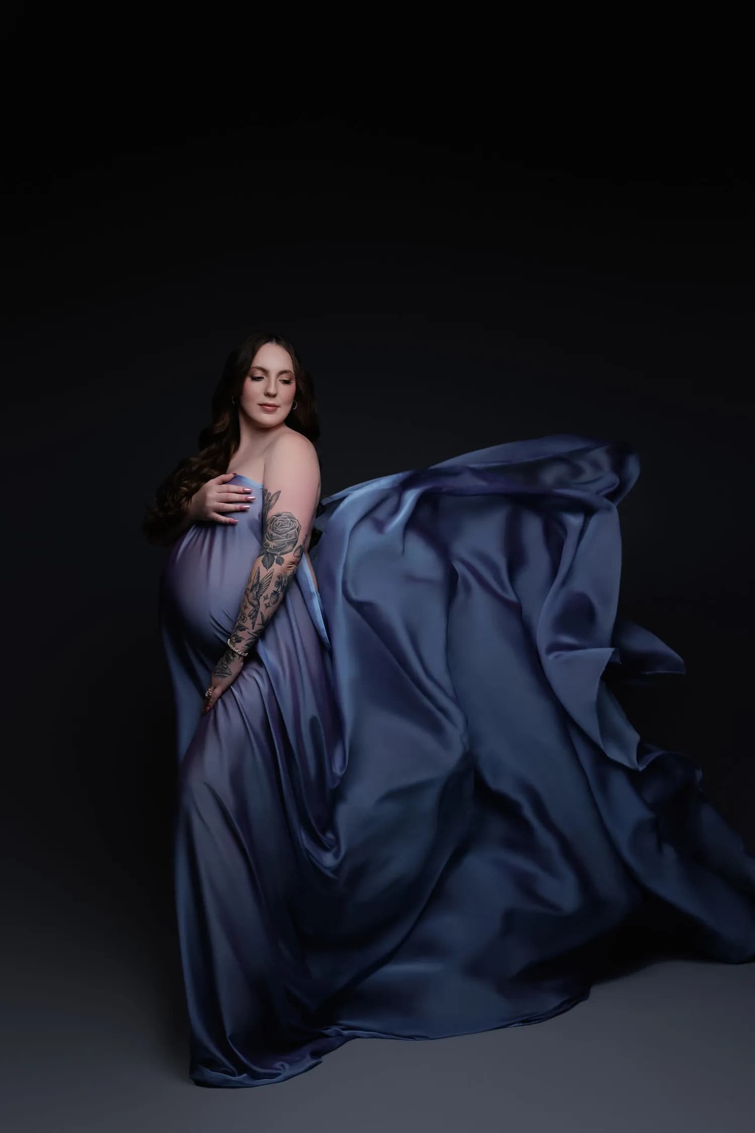 Pregnant woman in blue satin with the fabric billowing to one side