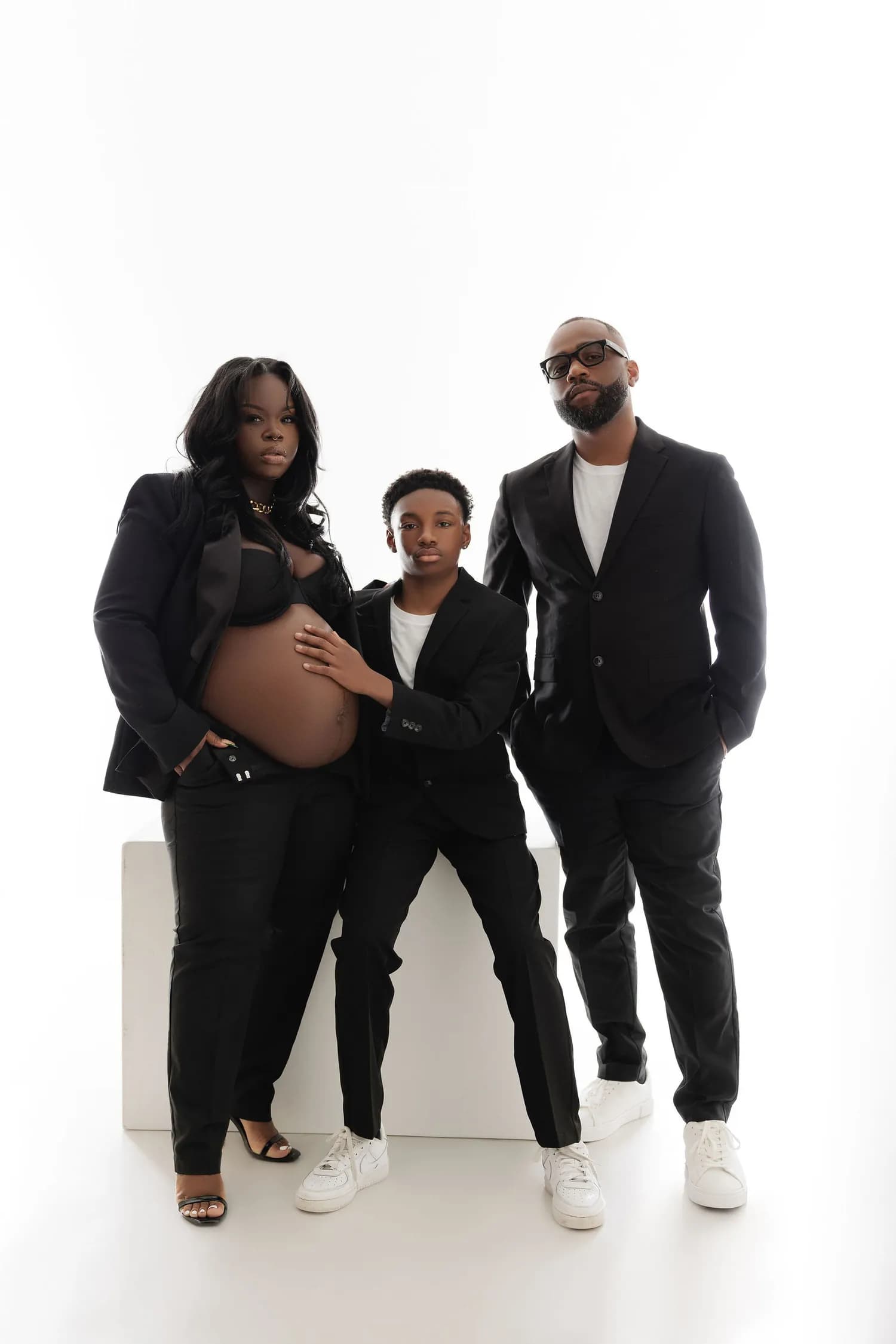 Pregnant woman with her partner and a boy, all in black suits, on a white background