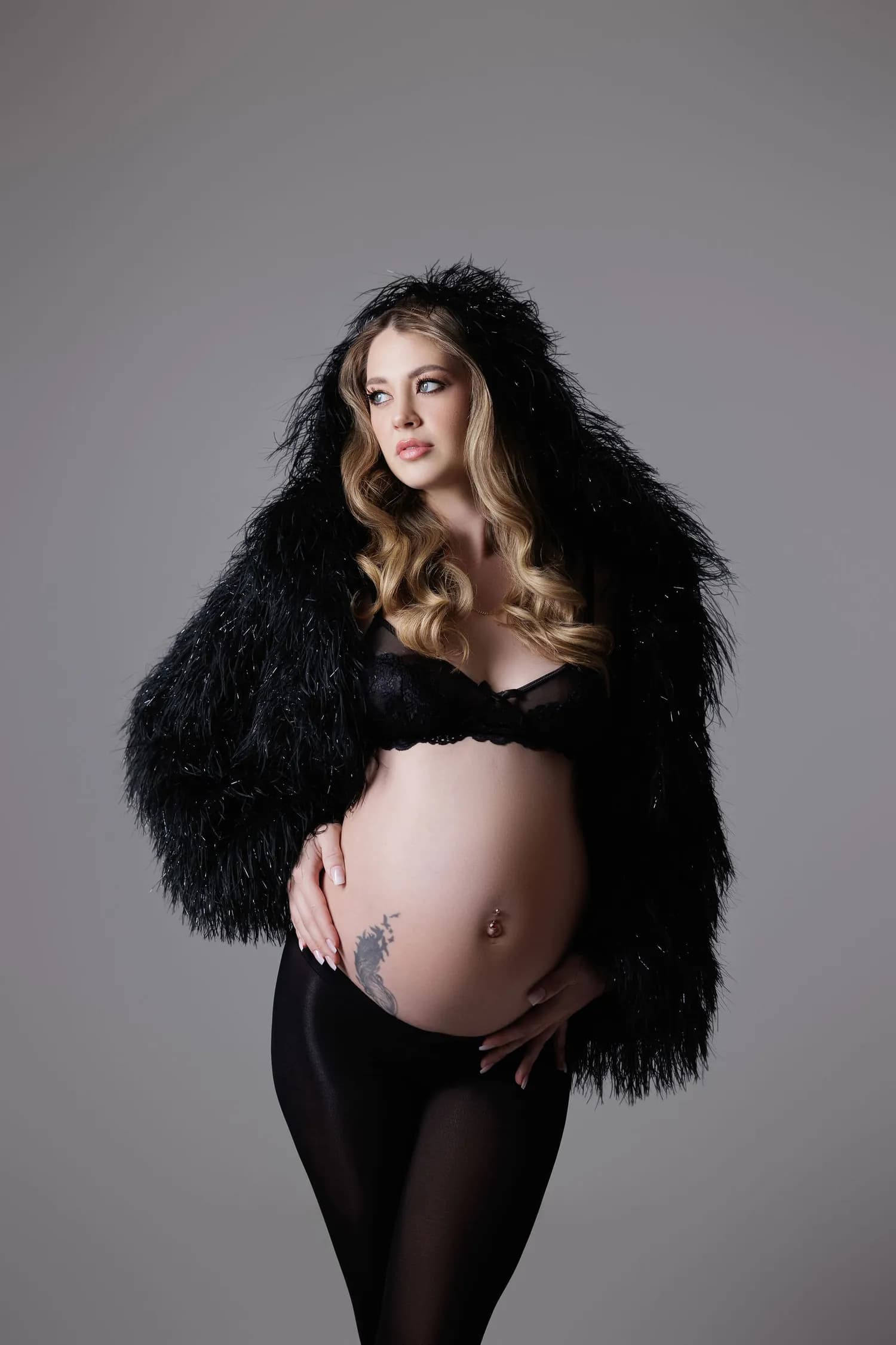 Pregnant woman in a black faux-fur jacket against a grey backdrop