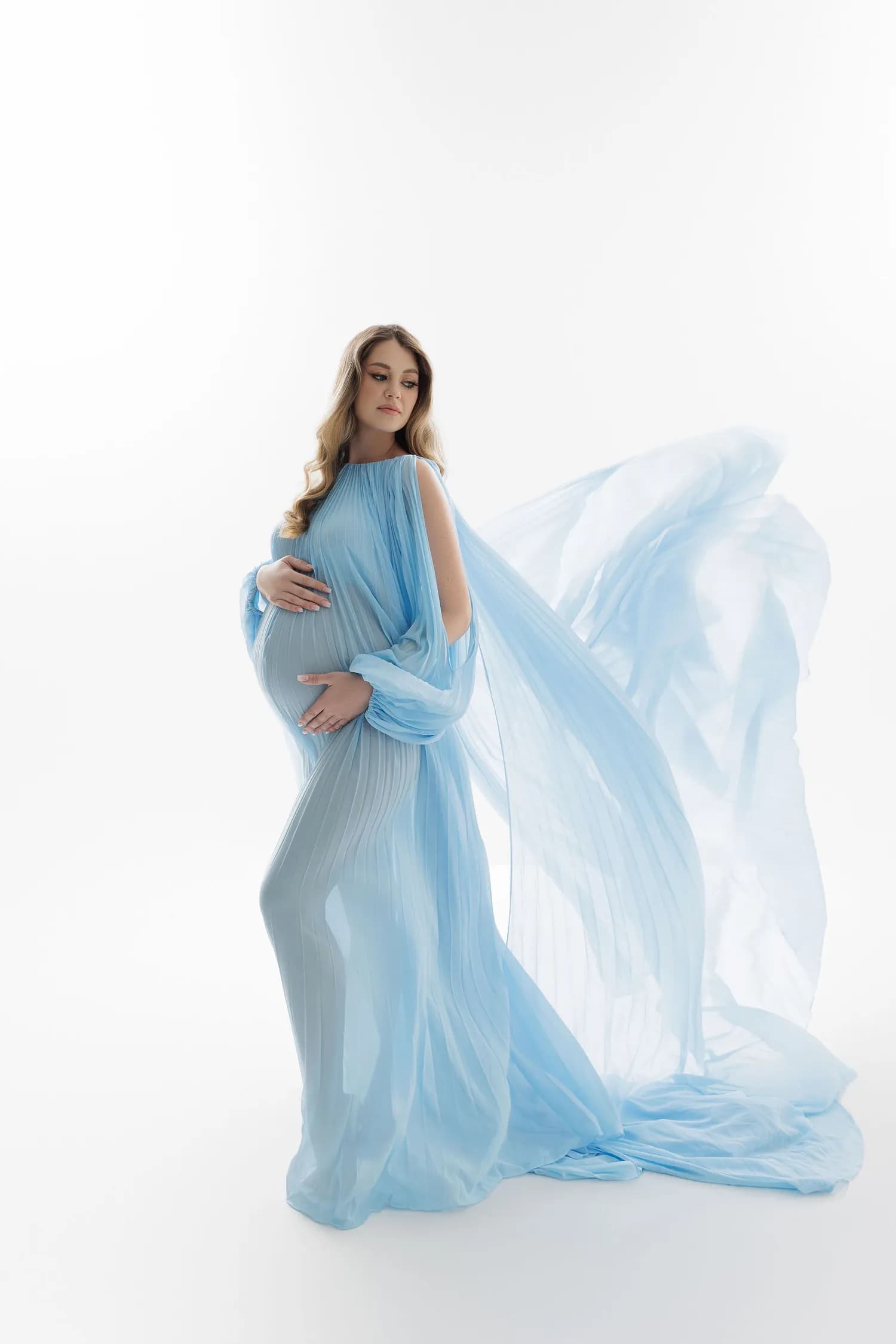 Pregnant woman in pale blue chiffon with the fabric floating behind her