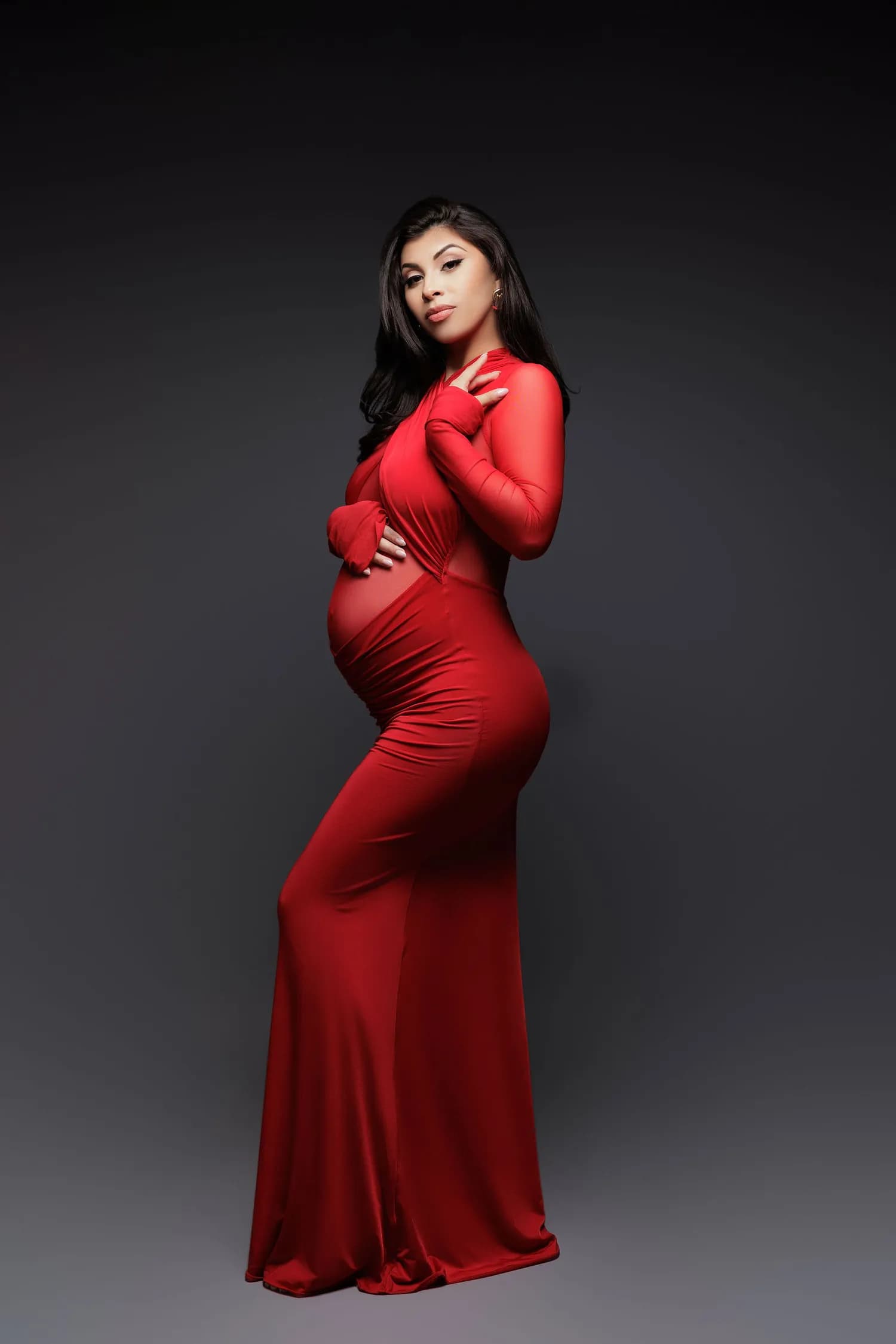 Pregnant woman in a fitted red long-sleeved gown, looking at the camera