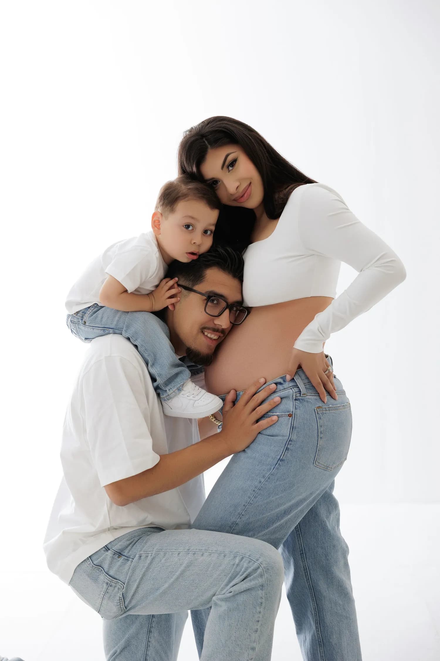 Man kneeling with his ear to the bump while a little boy rides on his shoulders