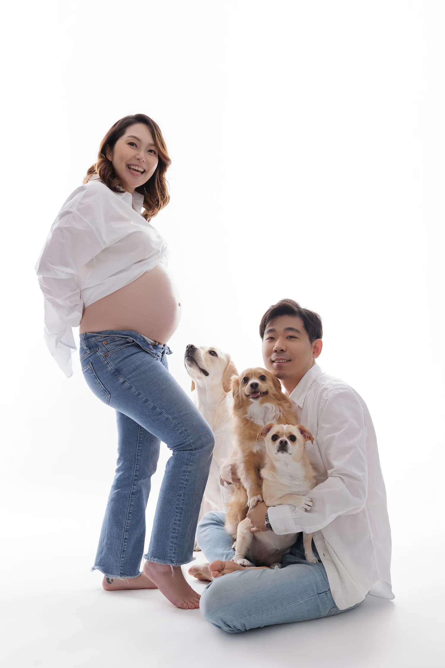 A laughing pregnant woman beside a man holding three small dogs