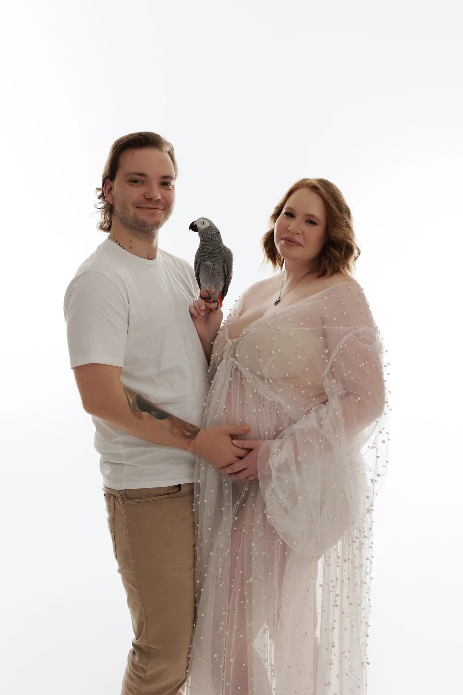 An expecting couple on a white background, an African gray parrot on his hand