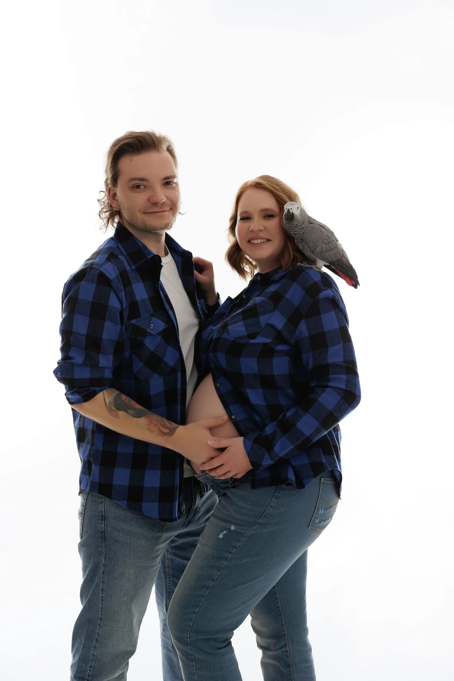 An expecting couple in matching plaid shirts, an African gray parrot on her shoulder